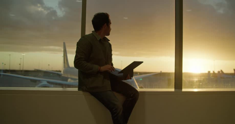 A man is sitting at an airport and looking at a laptop