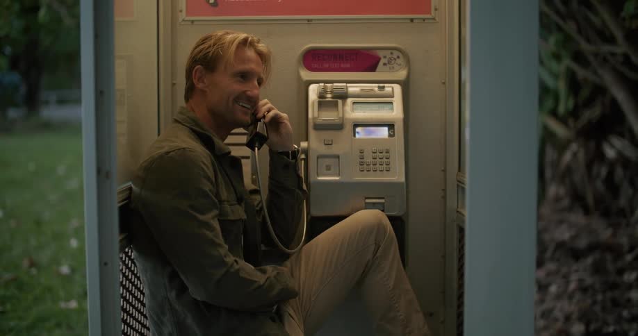 A man is talking on the phone at a phone booth