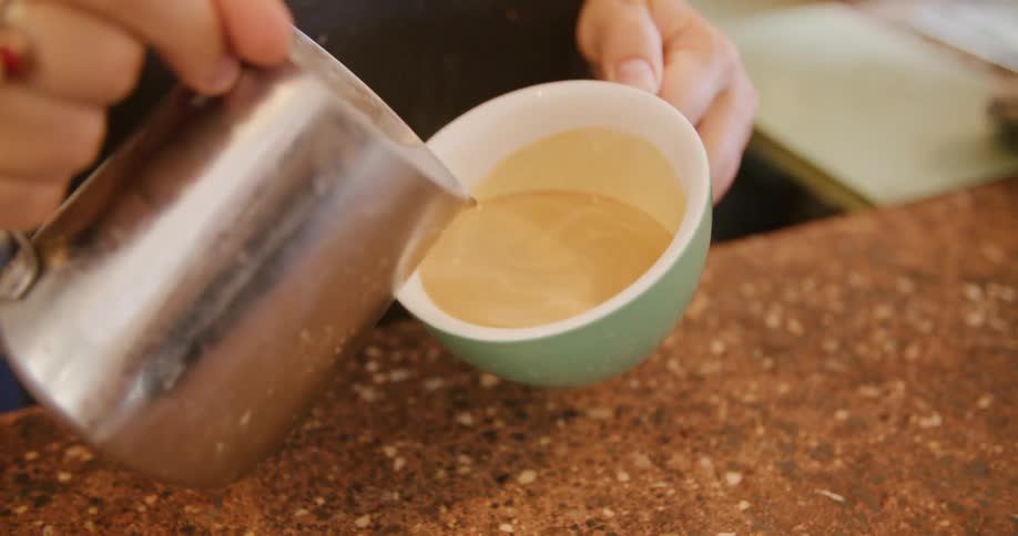 A person pours cream in their coffee