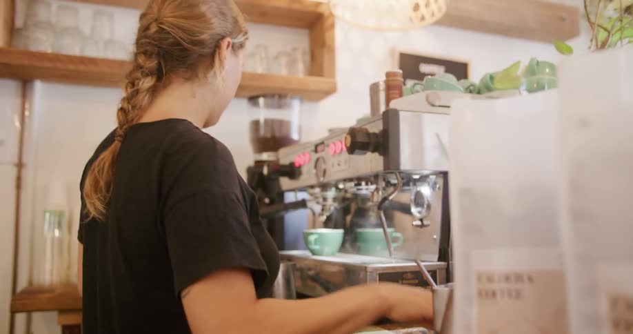 A barista uses a coffee machine to prepare drinks in a cafe