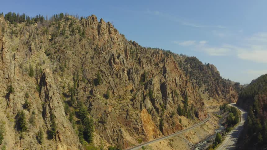 Red vehicle drives along highway hugging forest covered mountain slope across ravine from train train tracks hugging another mountain
