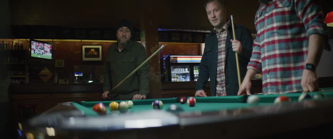 Man shooting pool while his friends watch at bar