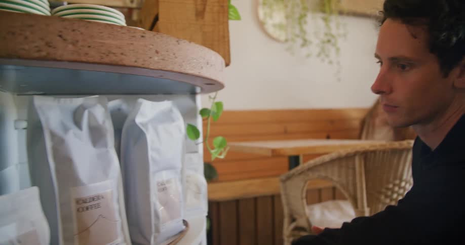 Young man reading the back of a bag of coffee on the shelf inside a restaurant