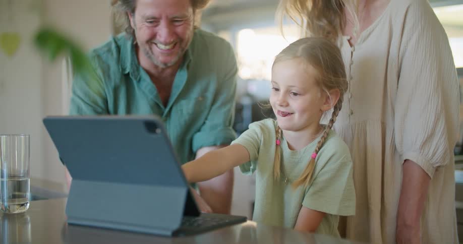 Father with beard blue shirt daughter with braids and blonde mother wearing brown dress use and look at tablet in kitchen at home