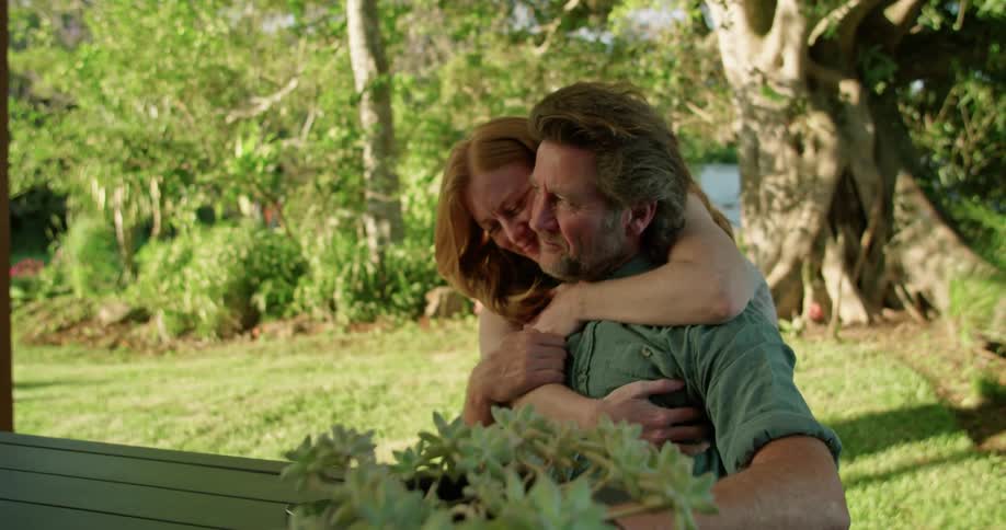 A woman walks up to a man sitting on the shore and hugs him and kisses him
