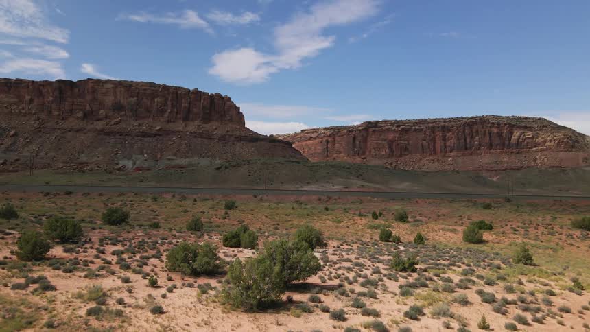 Desert with plants and mesas and a few clouds in the sky