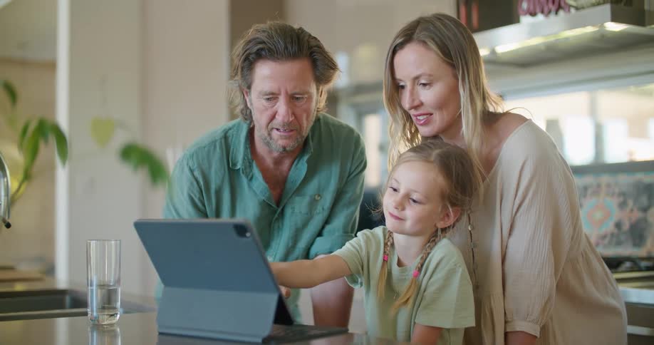A couple help their daughter as she uses a touchscreen laptop in their kitchen