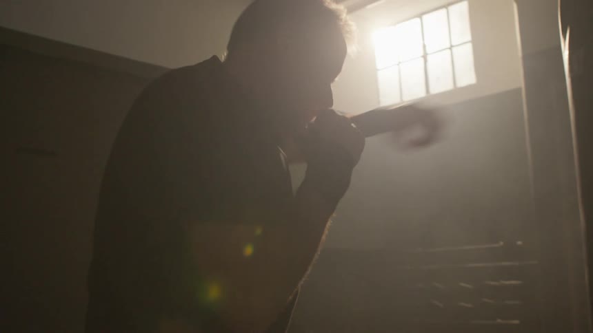 Man shadow boxes while standing in dimly lit gym near punching body bag