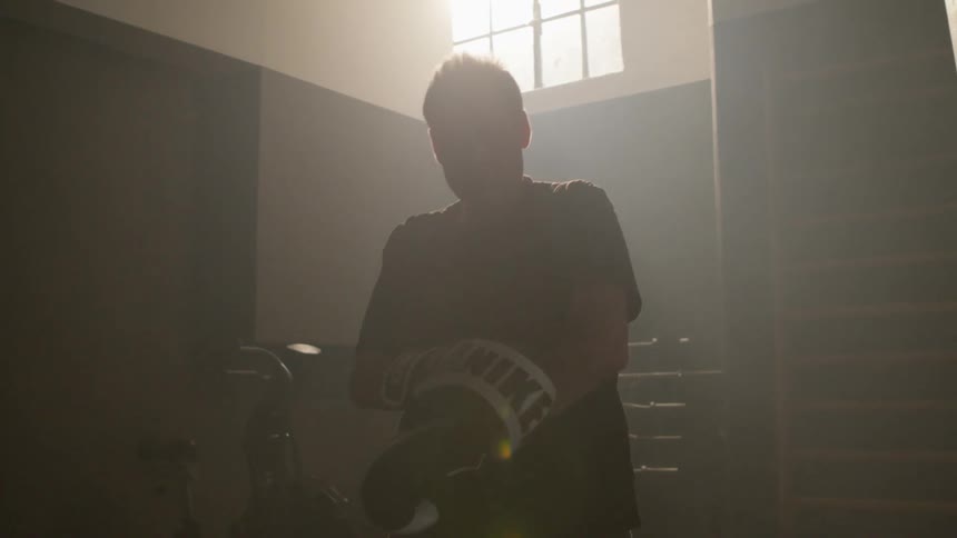 A man finishes punching the heavy bag and removes his boxing gloves