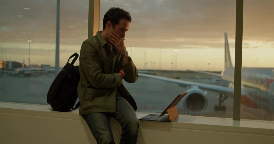 Man working on laptop sitting on a ledge near a window at the airport