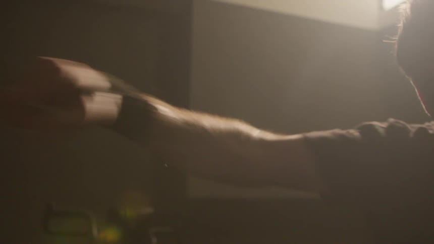 Sunlight filters through a window over a man shadow boxing on a dimly lit gym at morning