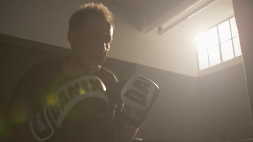 Man wearing boxing gloves hits the bag in dimly lit gym