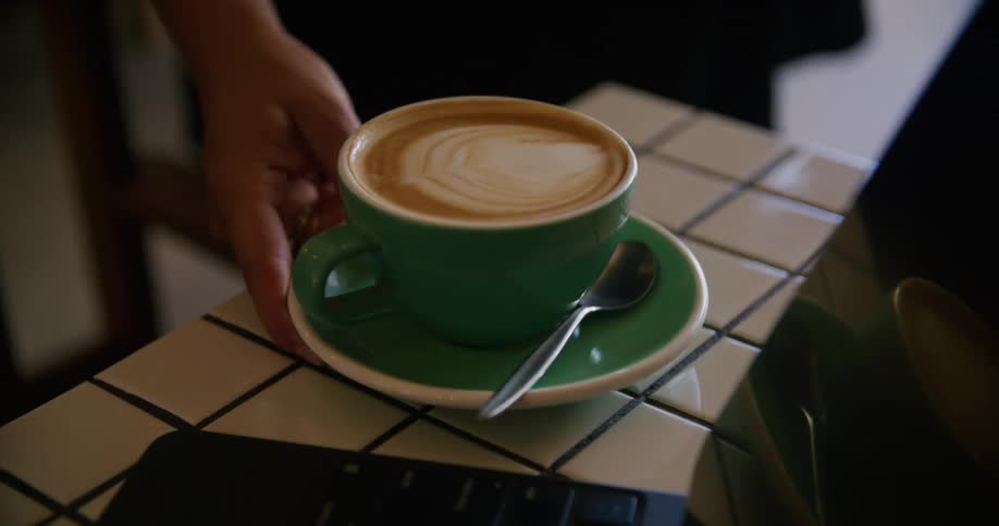 A waitress places a cappuccino cup with cream art onto table