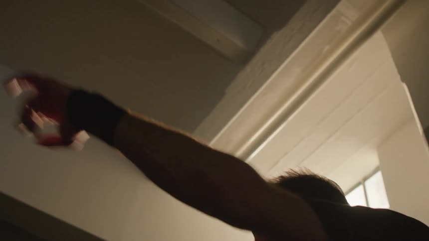 Sunlight filters through a window over a man shadow boxing on a dimly lit gym at morning