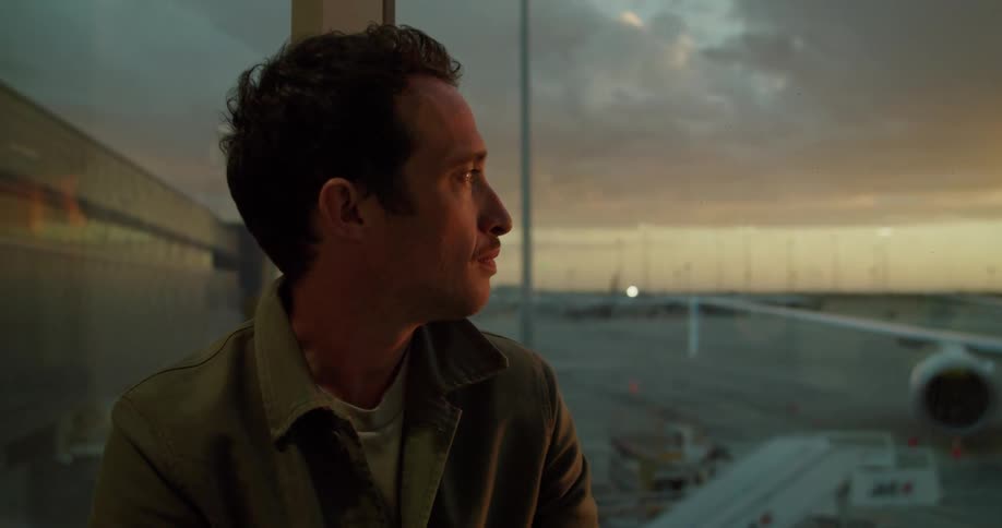 Man sits near window typing on tablet with airplane on tarmac in the background