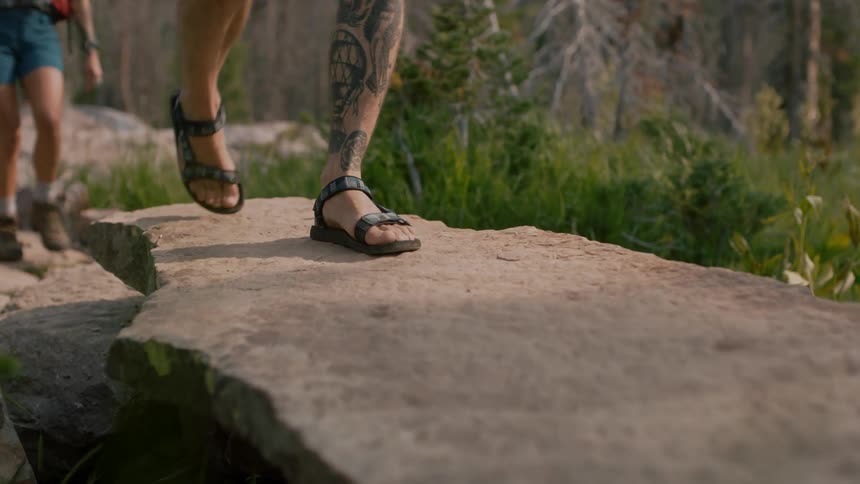 Couple walking on a rocky trail through the forest with a black dog