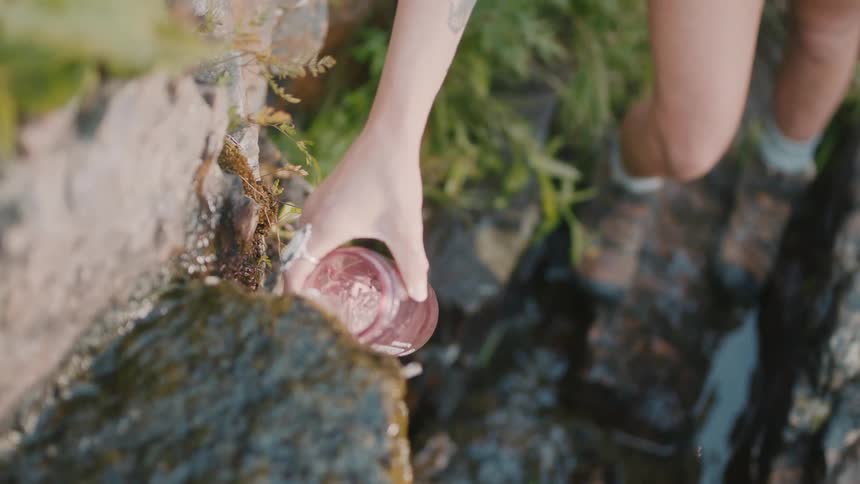 Woman on a hike fills up a water bottle from a stream or fountain