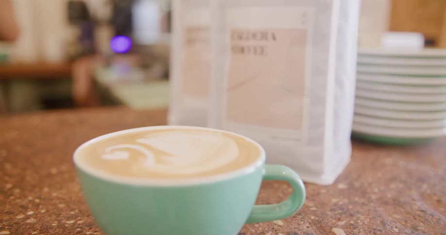 Freshly made latte sitting in front of coffee bags on a counter