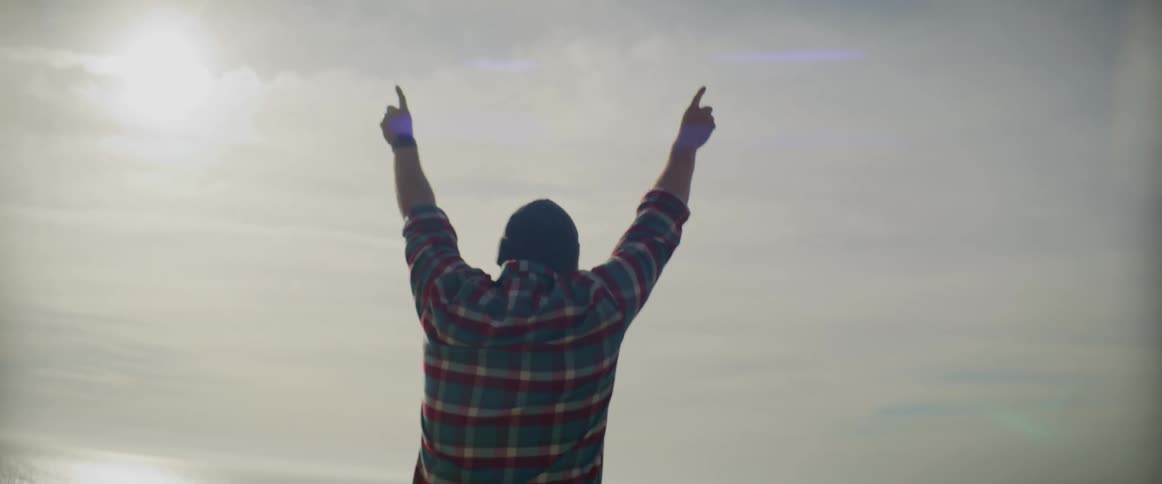 Man sits top of seat in parked convertible reaching his hands to the sky as his friends sit in the front