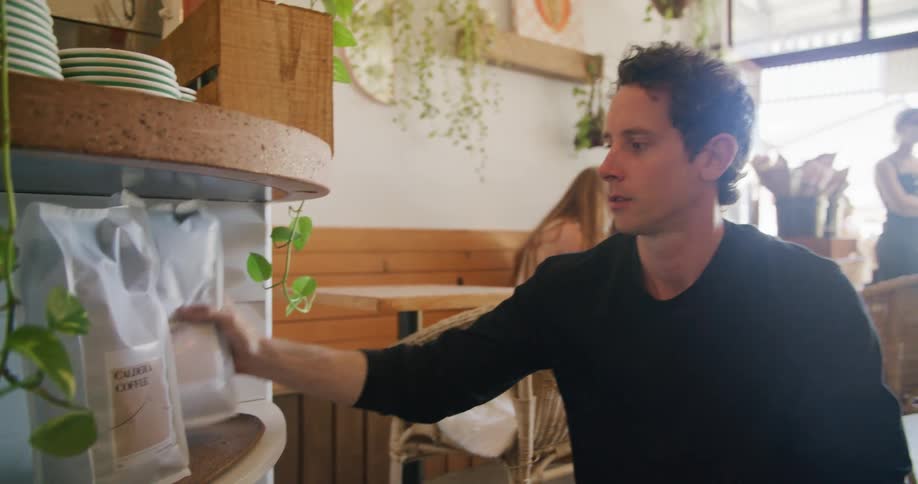Man setting out coffee bags on display on shelf at a coffee house