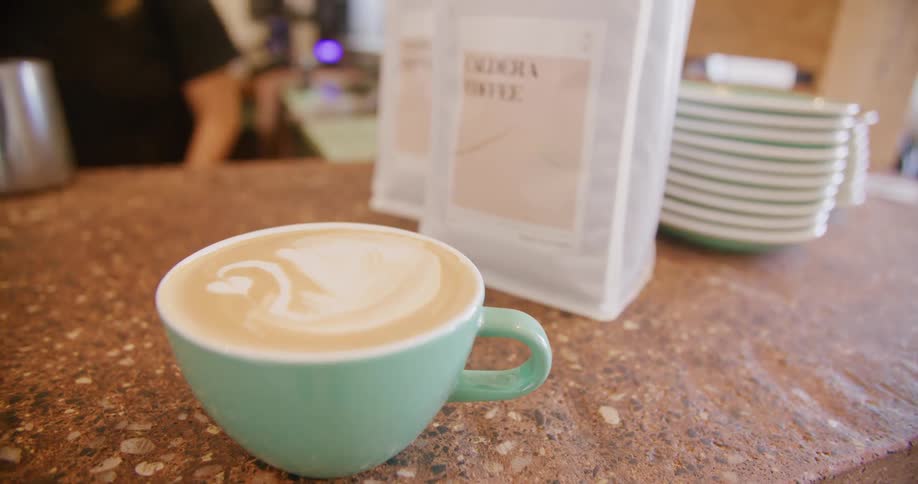 A latte in a green mug rests on the counter of a coffee shop