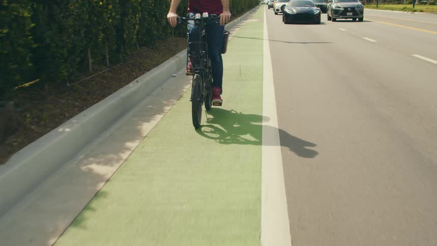 A biker and cars are moving in the same direction on a street in spring