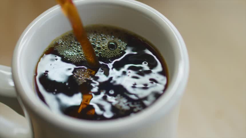 Coffee is being poured into a white cup