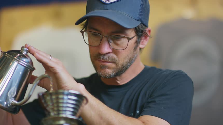 A shop owner filling up a container with hot water using a small teapot