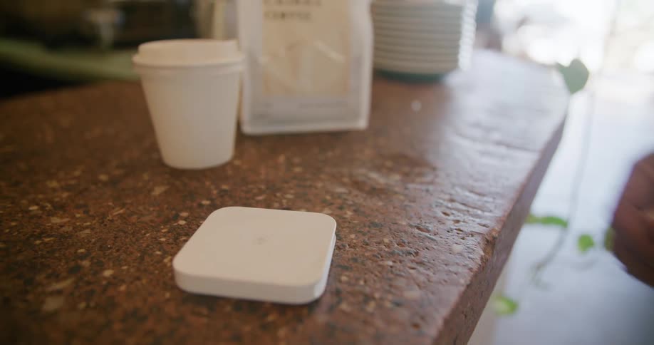 A man scans his card and picks up his coffee and a bag at a cafe