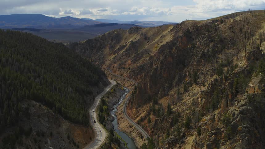 Vehicles driving on a road near a river close to train tracks on a canyon between the mountains