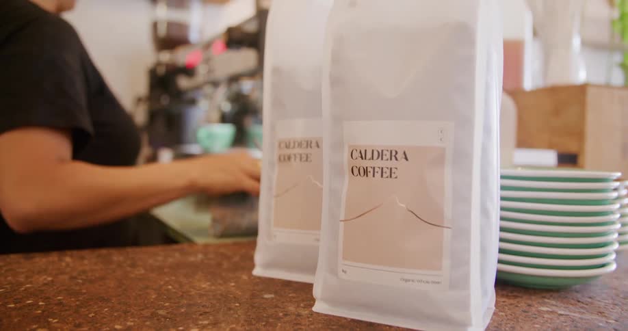 Barista prepares coffee on an espresso machine in front of bags of ground coffee