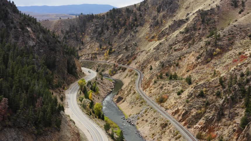 Aerial view of cars driving on a road near a river close to a railway on a canyon in the mountains