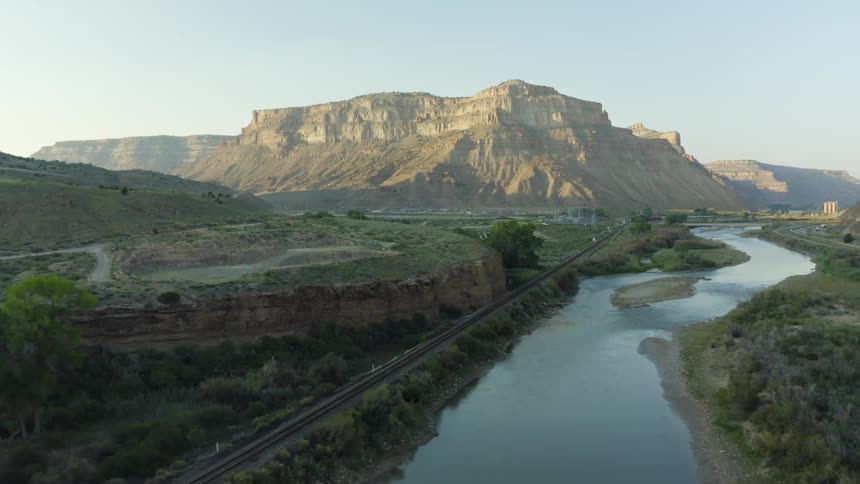 Aerial view of a train track near a river in the plains near the mountains at morning