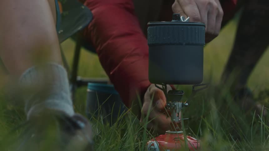 Person uses a lighter to turn on a camping gas stove over the grass outdoors