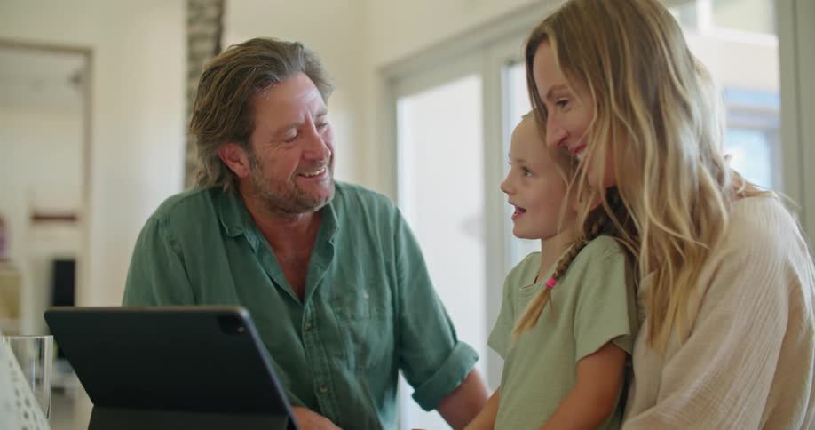 A child stands in front of her mother and smiles as her dad shows her something on a tablet