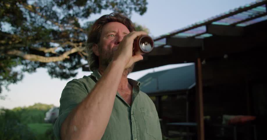 Middle aged emotional man drinks beer next to country house in the countryside