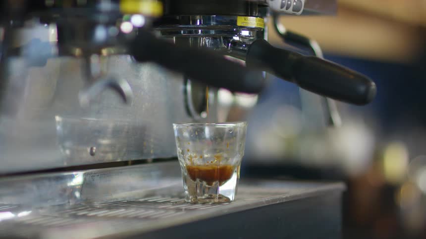 Hot brewed coffee being poured on a small glass resting on the espresso machine