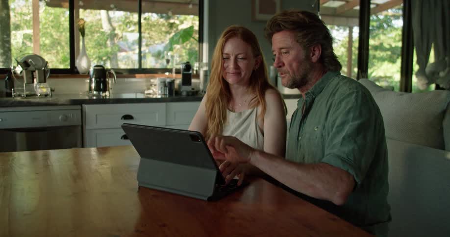 A happy couple sitting in a kitchen working together on an ipad