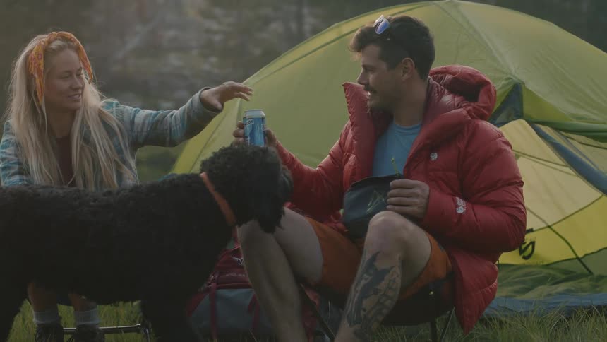 Husband and wife are camping together in the woods with their dog
