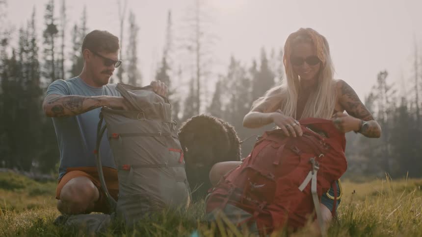 A couple unpack their backpacks as their dog watches on
