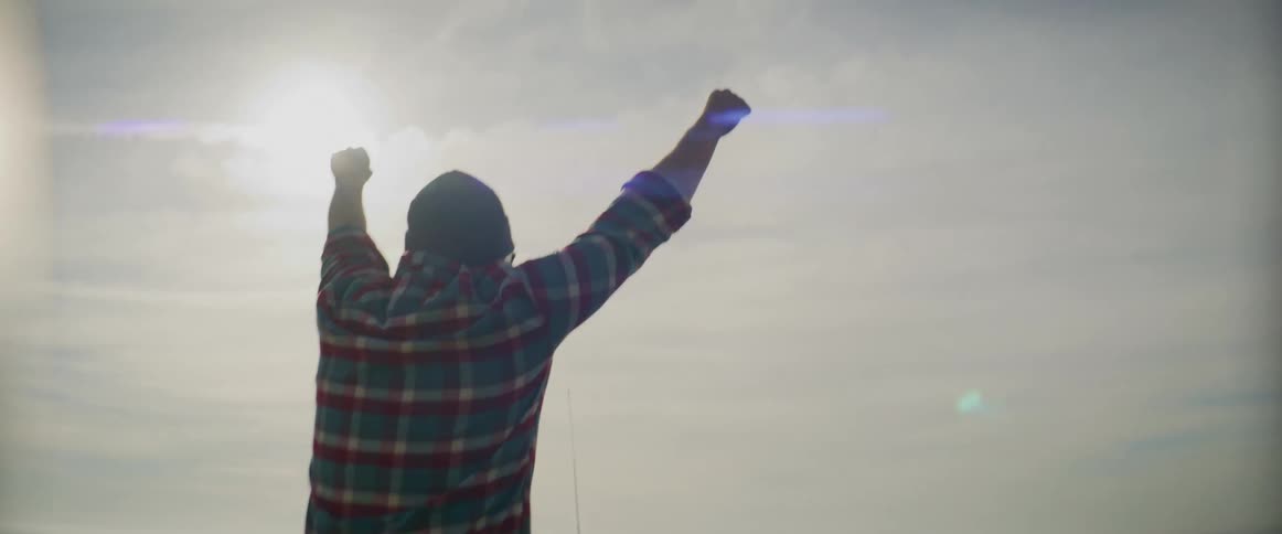 A man is raising his arms in the air sitting in the convertible
