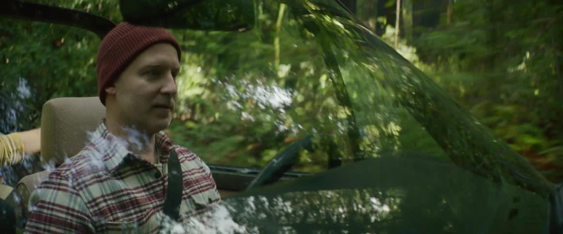 Man wearing a red beanie driving a car on a road through the forest at morning
