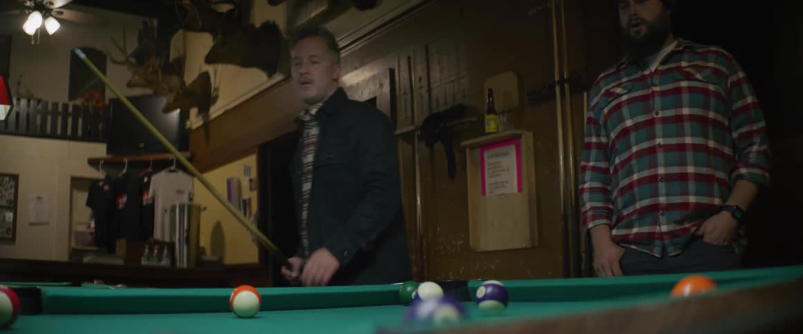 Man watches another man make shot on pool table
