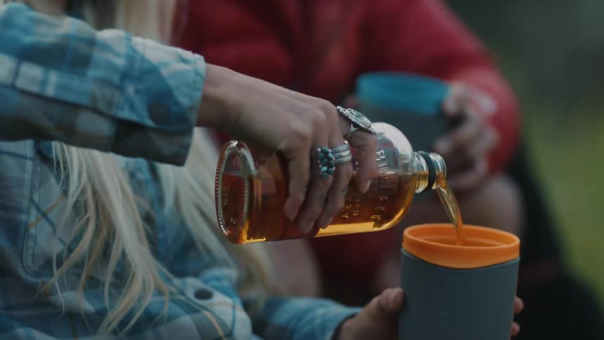 Man and woman are drinking a beverage while camping outdoors