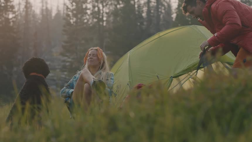 Man and woman are camping in a wooded area with their dog