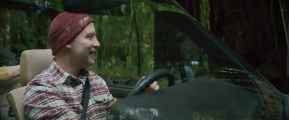 A man smiles and talks as he drives through the woods following trail signs