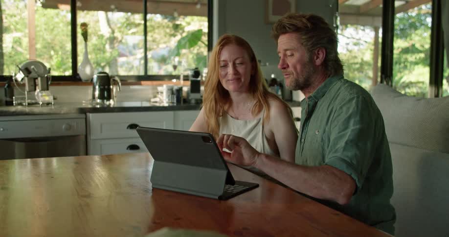 A man and woman sitting in a house talking in front of a tablet