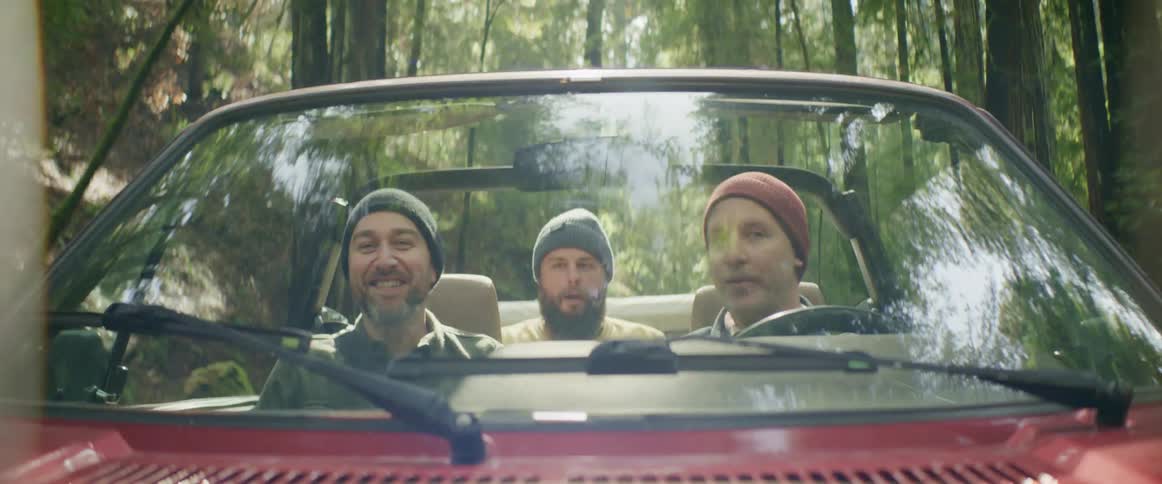 Group of friends talking while driving on a red convertible car through the forest