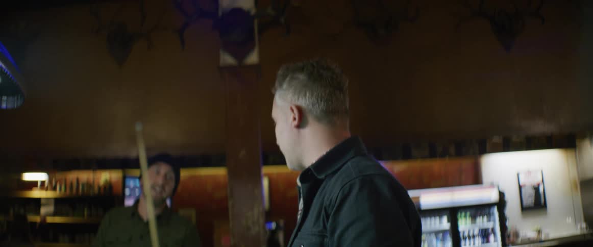 Man standing in gaming room hands pool cue to another man