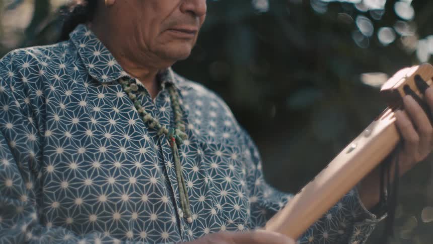 Man stands outdoors examining wooden musical instrument